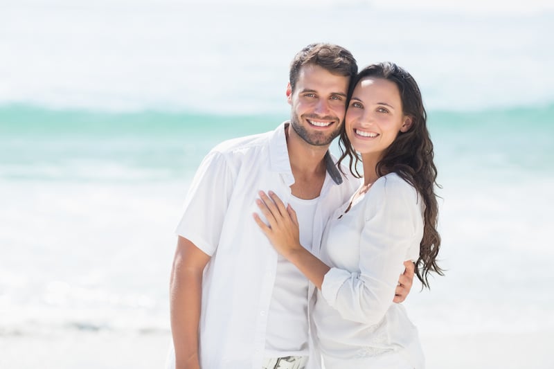 Smiling couple on beach, both with beautiful teeth because of regular dental visits