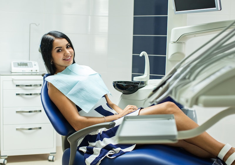 Young brunette woman smiling while sitting in a dental chair, happy her dentist uses the latest, most comfortable technology