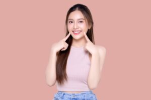 young Asian woman pointing finger to her teeth on isolated pink background.