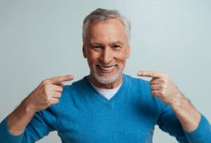 Smiling senior man points to his new permanent dentures