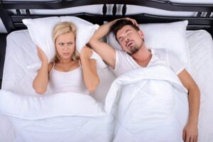 Couple in bed, woman is covering a pillow to her ears as the man is asleep